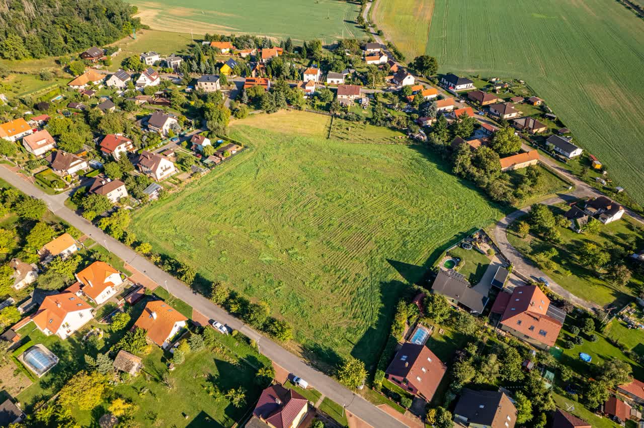 Pohled z dronu na louku a parcely obklopené domy a zahradami